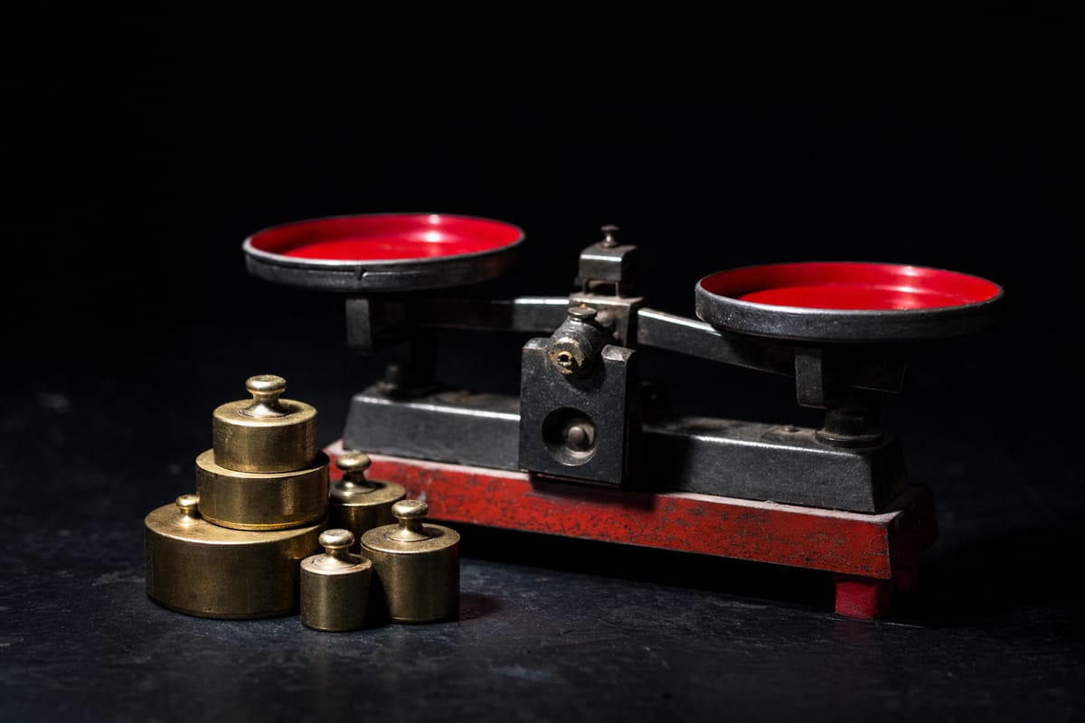 Brass weights stacked beside a balance-beam scale on a dark table under a spotlight (AI-generated image)