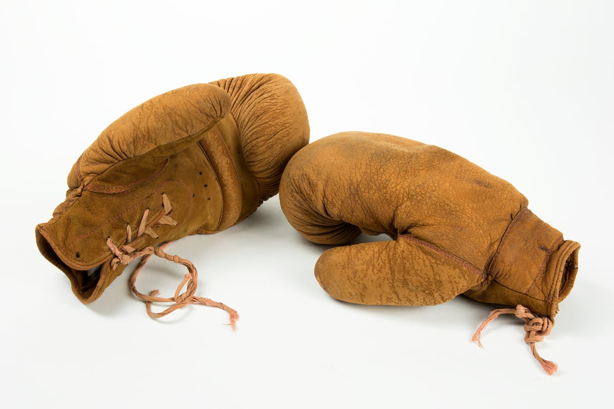 Pair of brown 1930s leather boxing gloves with frayed laces on a white background