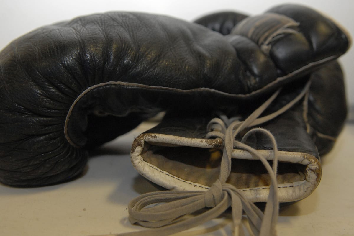 Worn pair of black lace-up boxing gloves with white cuffs lying on a table
