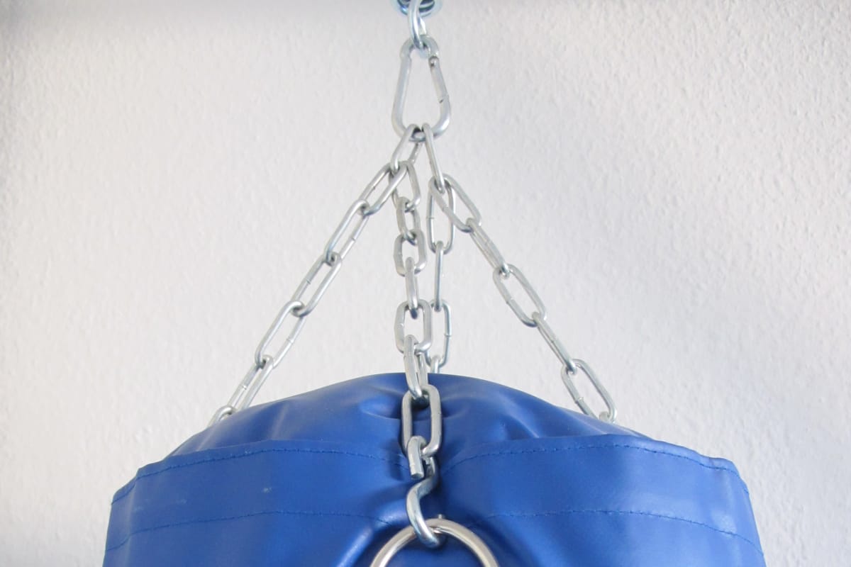 Blue heavy punch bag hanging from steel chains against a white wall
